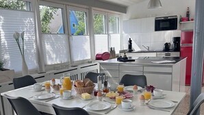 A modern kitchen with white cabinets, a red refrigerator, and a dining area with a white table set for breakfast.