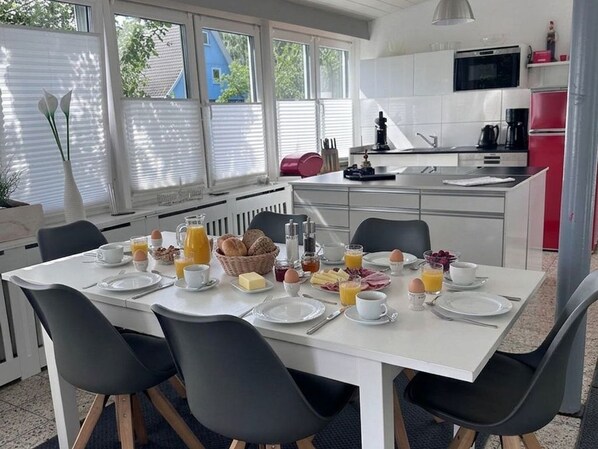 A modern kitchen with white cabinets, a red refrigerator, and a dining area with a white table set for breakfast.