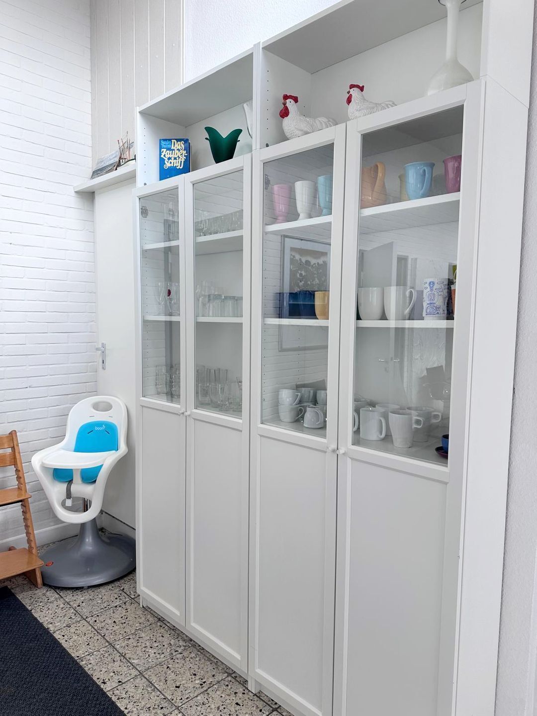 A white cabinet with glass doors containing various kitchenware.