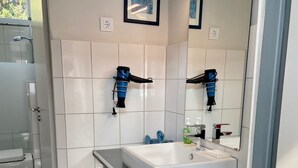 A modern bathroom with a white sink, a large mirror, and two hair dryers mounted on the wall.