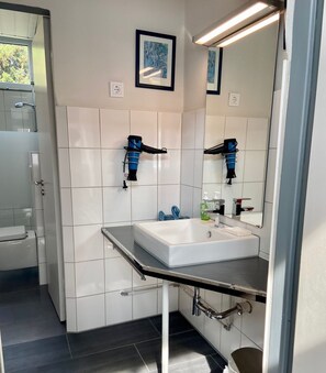 Un baño moderno con un lavabo blanco, un espejo grande y dos secadores de pelo fijados a la pared.