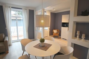 A modern living room with a round dining table, white chairs, a hanging light fixture, and a view of a balcony through large windows. - 1022- lighthouse Alte Da(h)me - new - lighthouse - Die Alte Dahme - new 1022 (Dahme)