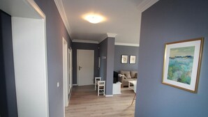 A hallway with a wooden floor, a white door, and a framed painting on the wall.