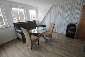 Quarto com mesa de vidro, duas cadeiras de vime, um sofá, lareira e janelas amplas.