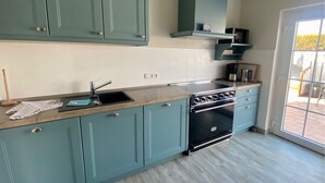 A kitchen with teal cabinets, a black stove, and a window to the right. - 4100 - Beach house 25 - 4100 - Beach house - An der Strandpromenade 25 (Dahme)