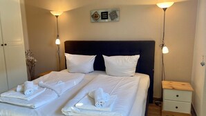 A neatly made bed with white linens and towels, a dark headboard, bedside tables with lamps, and a wall-mounted sign with the words 'love' and 'believe'. - 4100 - Beach house 25 - 4100 - Beach house - An der Strandpromenade 25 (Dahme)