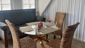 A modern living room with a glass-top coffee table, wicker chairs, a grey sofa, and striped wallpaper. - 4100 - Beach house 25 - 4100 - Beach house - An der Strandpromenade 25 (Dahme)