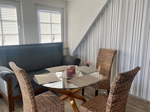 Ein modernes Wohnzimmer mit einem Glastisch, Korbstühlen, einem grauen Sofa und rahmig gestreifter Tapete.