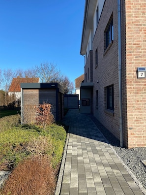 A modern building with a brick facade, a paved walkway, and a small garden area.