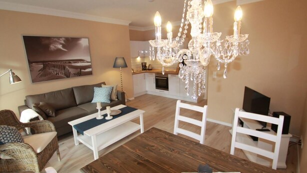 A living room with a wooden dining table, white chairs, a brown sofa, and a chandelier. - Beach shell - Alte Da(h)me - New 1024 - Beach shell - Die Alte Dahme - New (Dahme)