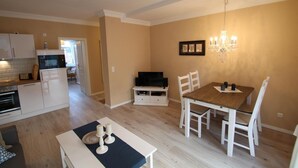 A modern kitchen with white cabinets, a built-in oven, and a microwave. There is a dining area with a wooden table and white chairs. - Beach shell - Alte Da(h)me - New 1024 - Beach shell - Die Alte Dahme - New (Dahme)