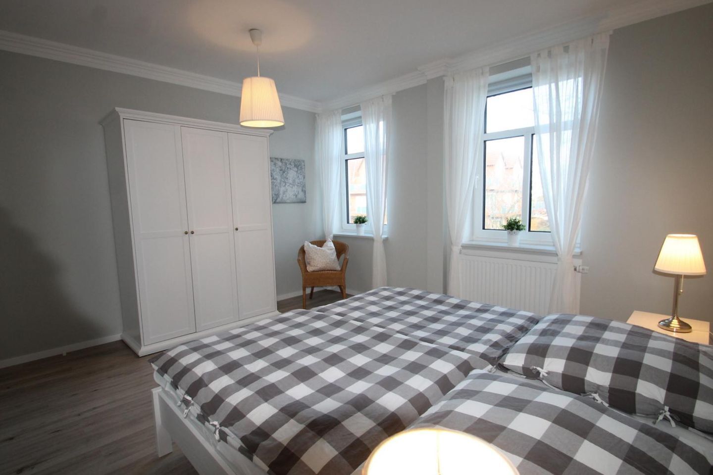 Een slaapkamer met een bed met ruitjesdeken, een kledingkast, een stoel en een raam met gordijnen.