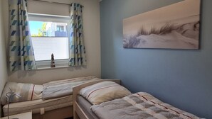 Quarto com duas camas, janela com cortinas, mesa de cabeceira com abajur e um quadro na parede.