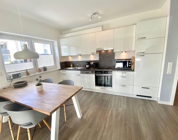 A modern kitchen with white cabinets, a wooden dining table, and a built-in oven.