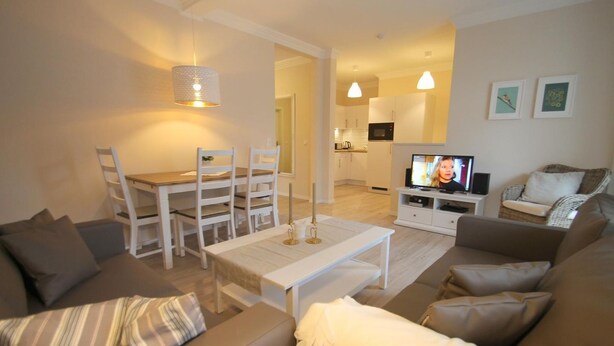 A modern living room with a dining area, a kitchen in the background, and a TV on a stand. - 1021- Strandzeit - Alte Da(h)me - New - Standzeit - Die Alte Dahme - New 1021 (Dahme)