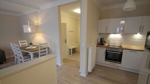 A modern kitchen with white cabinets, a wooden countertop, and a built-in oven. There is a dining area with a table and chairs, and a pendant light above the table. - 1021- Strandzeit - Alte Da(h)me - New - Standzeit - Die Alte Dahme - New 1021 (Dahme)
