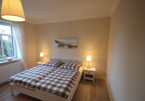 Una camera da letto con un letto, due comodini, una finestra con tende, un quadro appeso al muro e una lampada a sospensione.