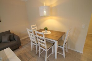 Un coin repas avec une table en bois, des chaises blanches, un luminaire suspendu et une petite plante en pot.