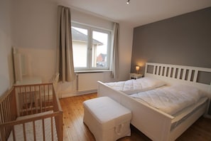 A bedroom with two beds, a window, a radiator, and a wooden crib. - 5070 - Groote Lüü - 5070 - "Groote Lüü" - Saarstrasse 15 (Dahme)
