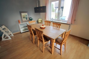 A dining area with a wooden table and chairs, a framed picture on the wall, and a window with curtains. - 5070 - Groote Lüü - 5070 - "Groote Lüü" - Saarstrasse 15 (Dahme)