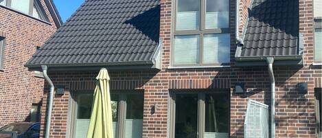 Een tweelaags bakstenen huis met een pannendak, een terras met tuinmeubilair en een schuifdeur van glas.