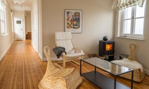 Una sala de estar acogedora con chimenea, una silla blanca, una silla de mimbre y una mesa de centro de vidrio.