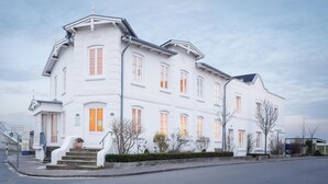En vit byggnad med många fönster och en trappa som leder upp till entrén.