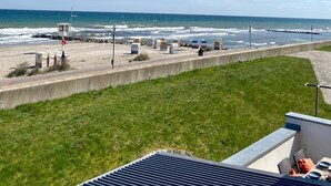 En strand med utsikt över havet, en livräddartorn, strandhytter och en gräsyta med en uteplats.
