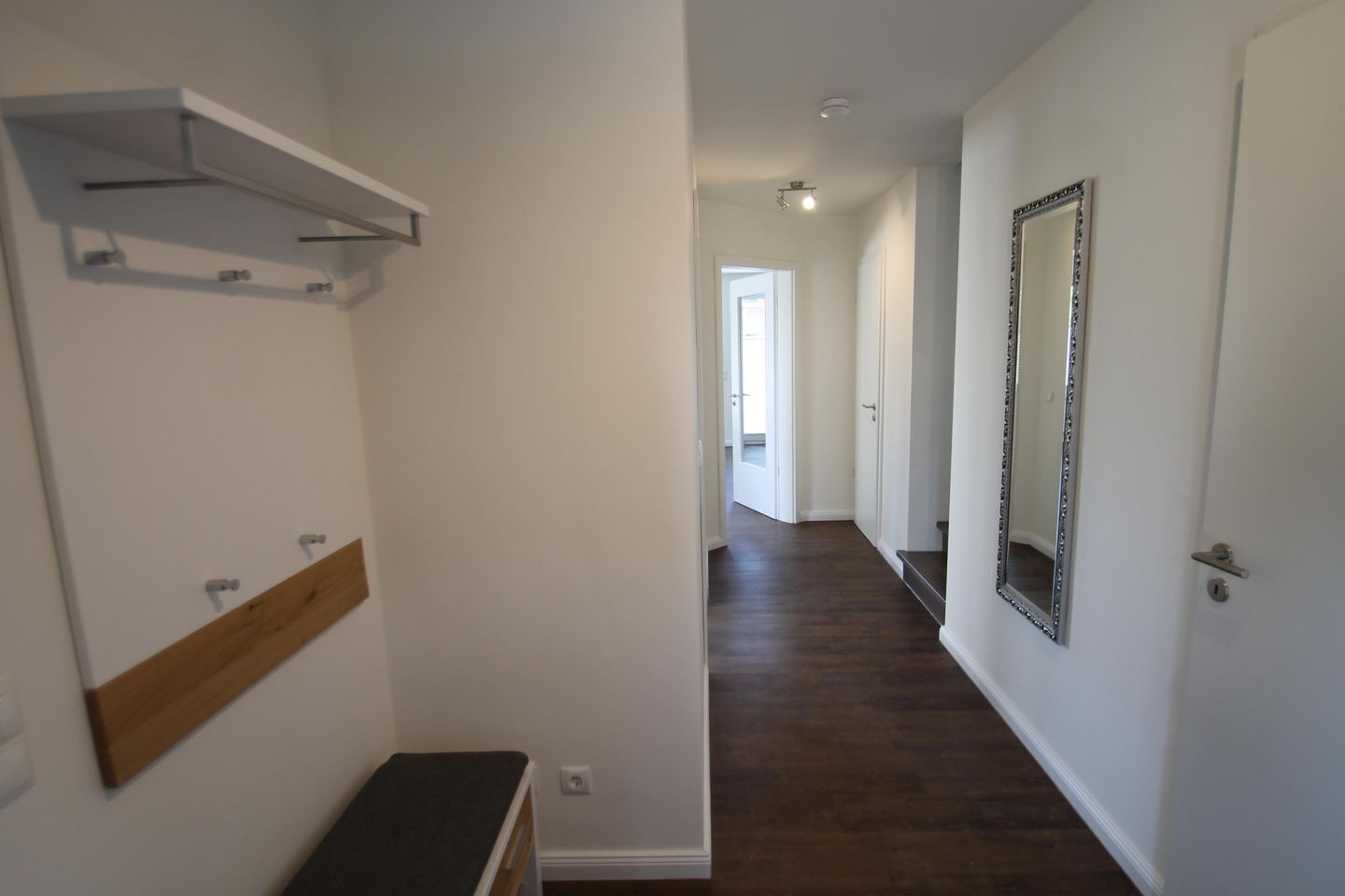 A hallway with a bench, a coat rack, a mirror, and a door.