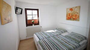 A bedroom with two beds, a window with blinds, a radiator, and a painting on the wall.