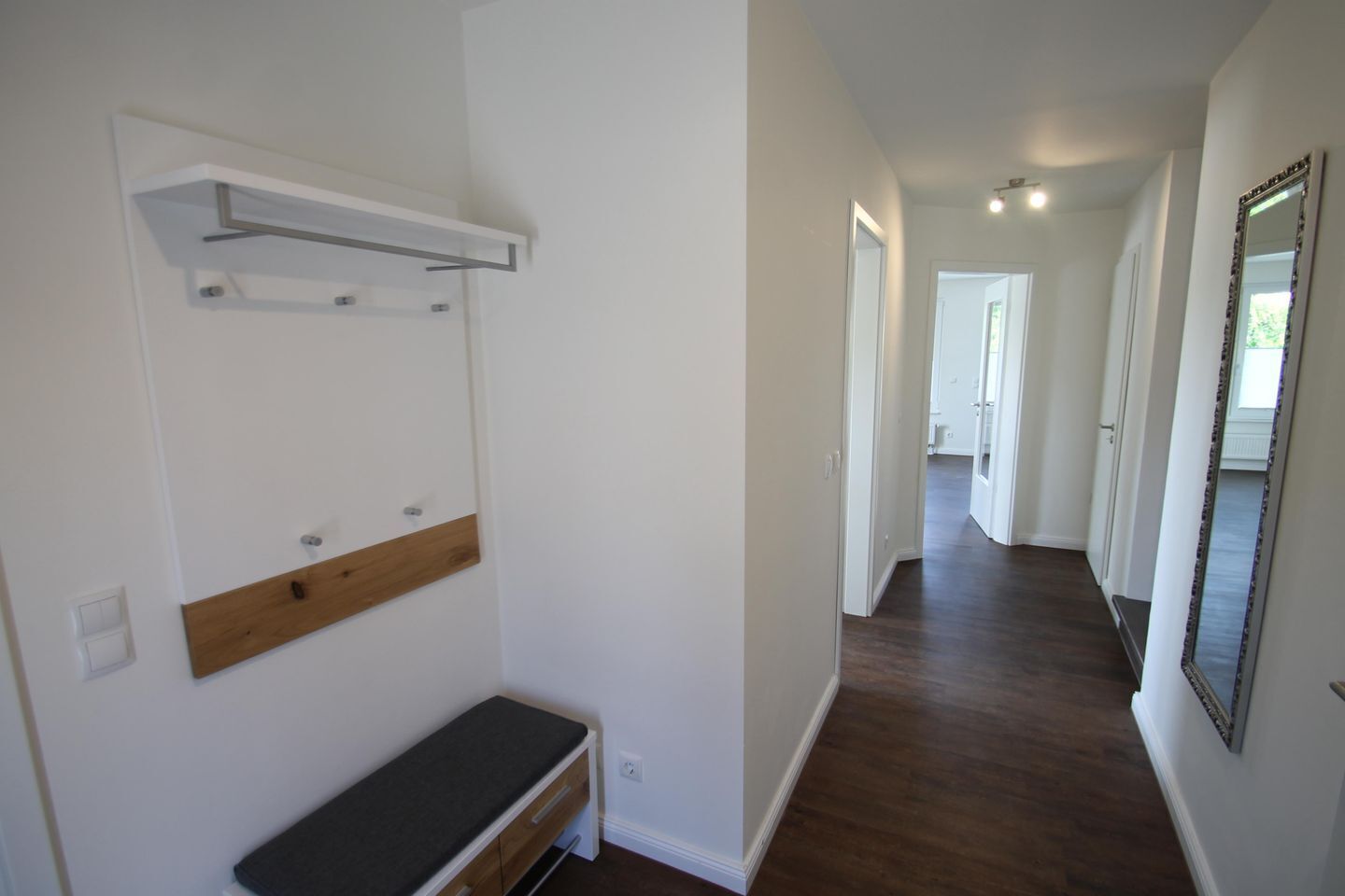 A hallway with a bench, a coat rack, and a mirror on the wall.