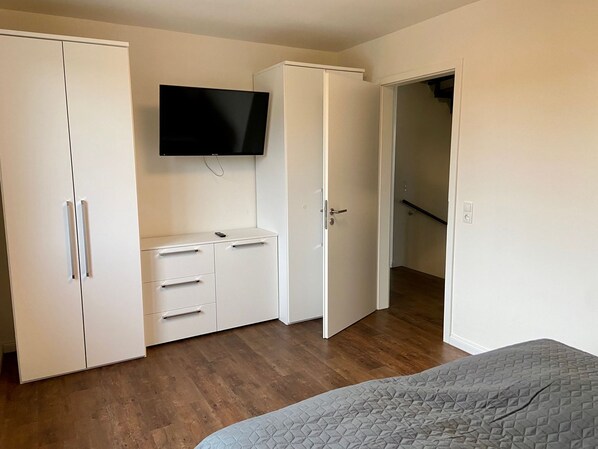 A bedroom with a bed, a wardrobe, a TV, and a door leading to a staircase.