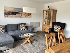 Una sala de estar moderna con un sofá seccional gris, una mesa de centro de vidrio, un aparador de madera y una mesa de comedor de madera con sillas.