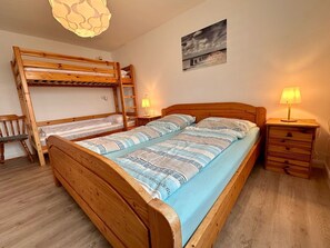 Habitación con literas, suelo de madera, mesita de noche con lámpara y un cuadro colgado en la pared.