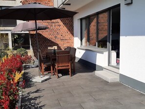Eine Terrasse im Freien mit Tisch, Stühlen und einem großen Sonnenschirm, an einer Backsteinmauer.