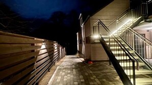 Vue nocturne de la façade d’un bâtiment, avec un chemin pavé de briques menant à un escalier.