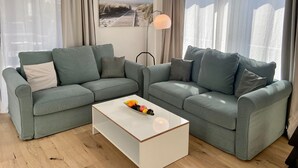 Un salon avec deux canapés gris, une table basse blanche ornée de fruits et un lampadaire.