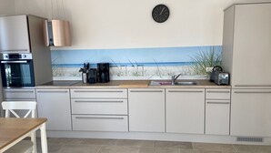 Une cuisine décorée d’une fresque représentant une plage, avec une horloge et des appareils électroménagers modernes.