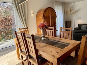 Ein Essbereich mit Holztisch, Stühlen, einer Blumenvase, einem Holzschrank und einer Couch.