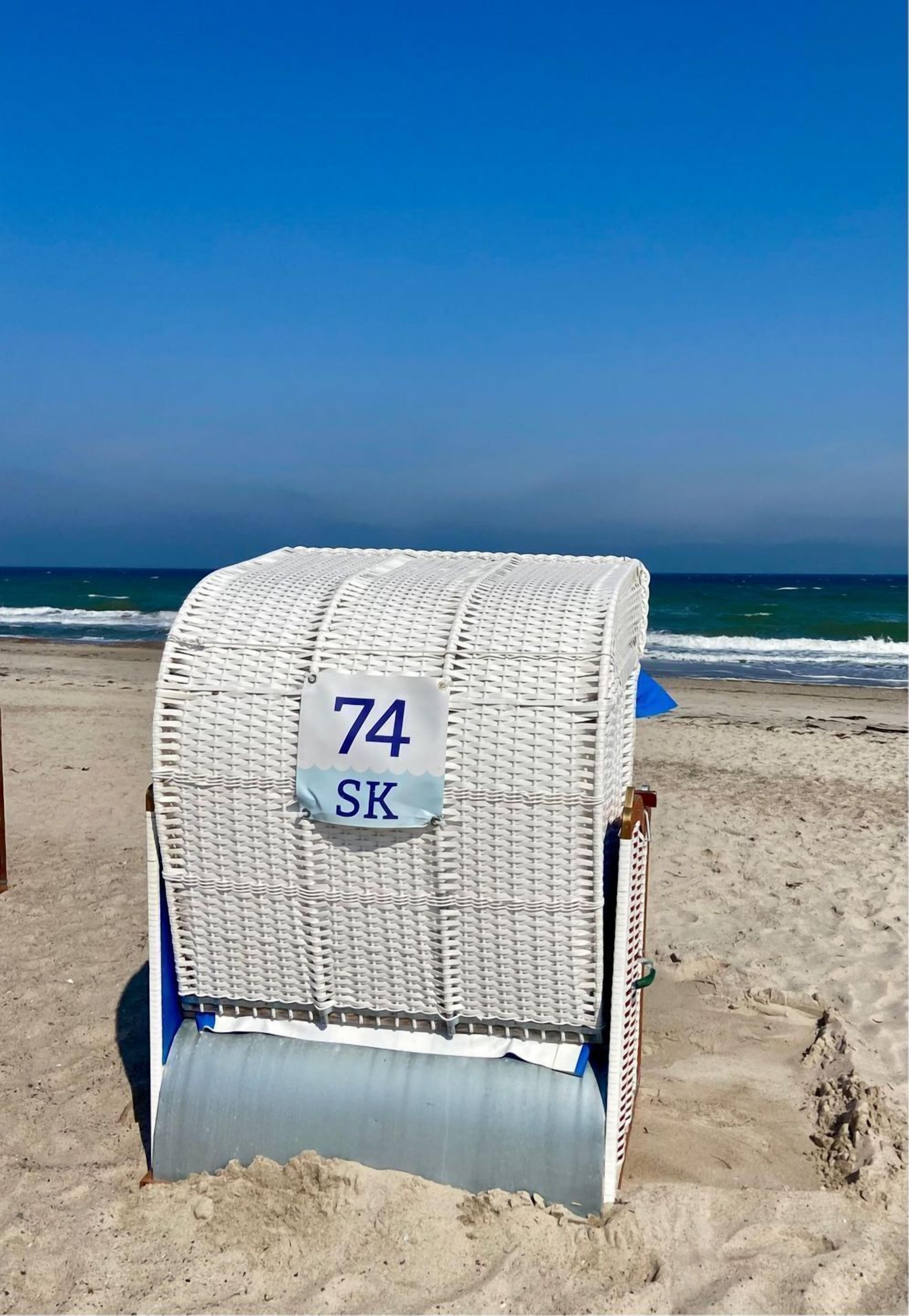 Une chaise de plage portant le numéro 74 SK, sur une plage de sable, avec l’océan en arrière-plan.