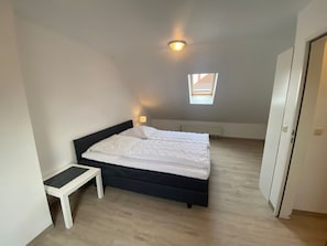 Une chambre à coucher avec un lit, une petite table de chevet, une fenêtre et un radiateur.