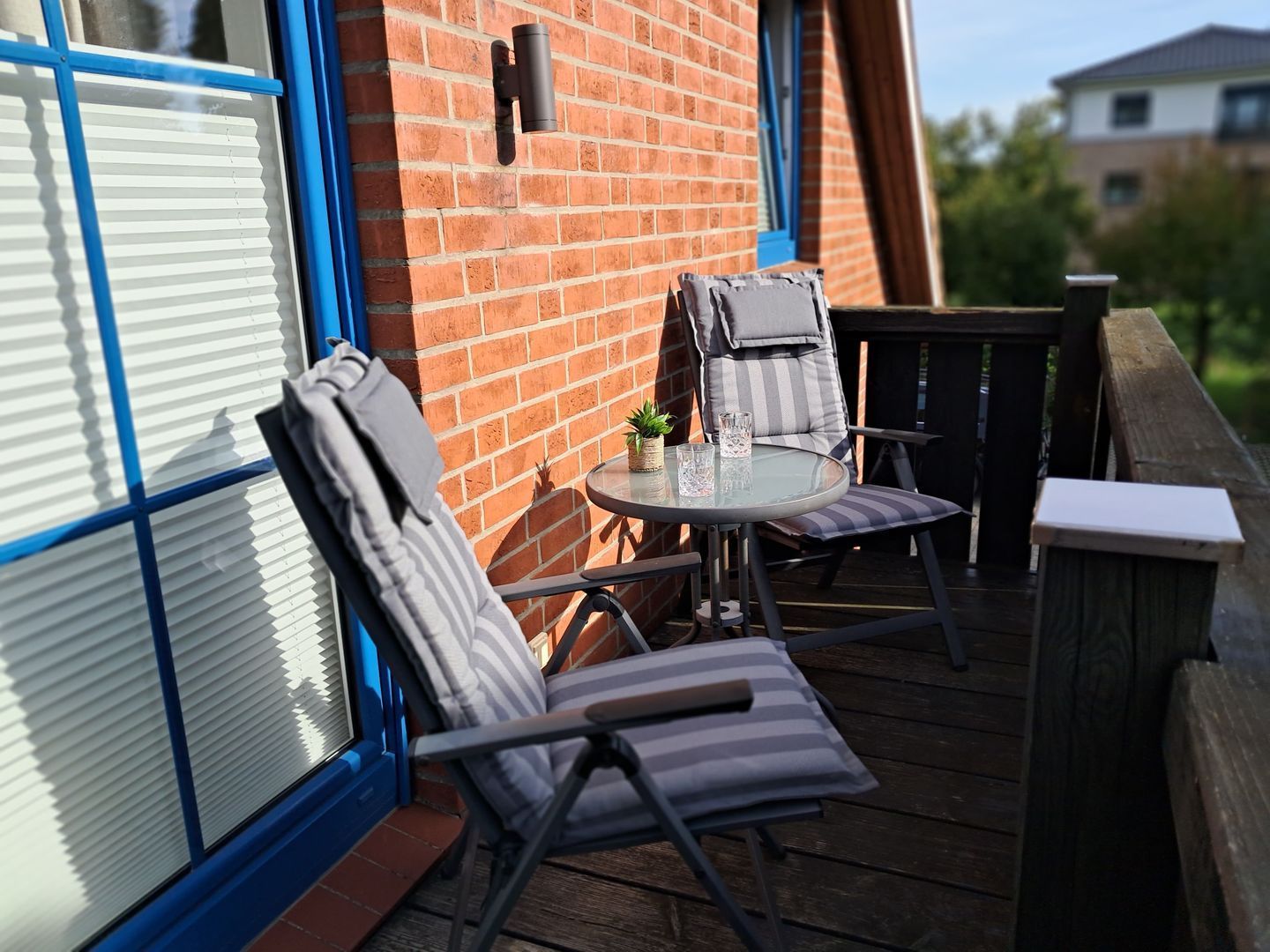 A patio with two chairs and a small table, a brick wall, and a window with blinds.