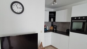 Una cucina moderna con mobili bianchi, forno integrato e una TV a schermo piatto su un mobile bianco.