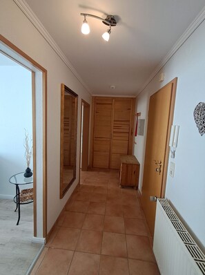 A hallway with a tiled floor, wooden doors, a small table with a vase, and a ceiling light fixture.