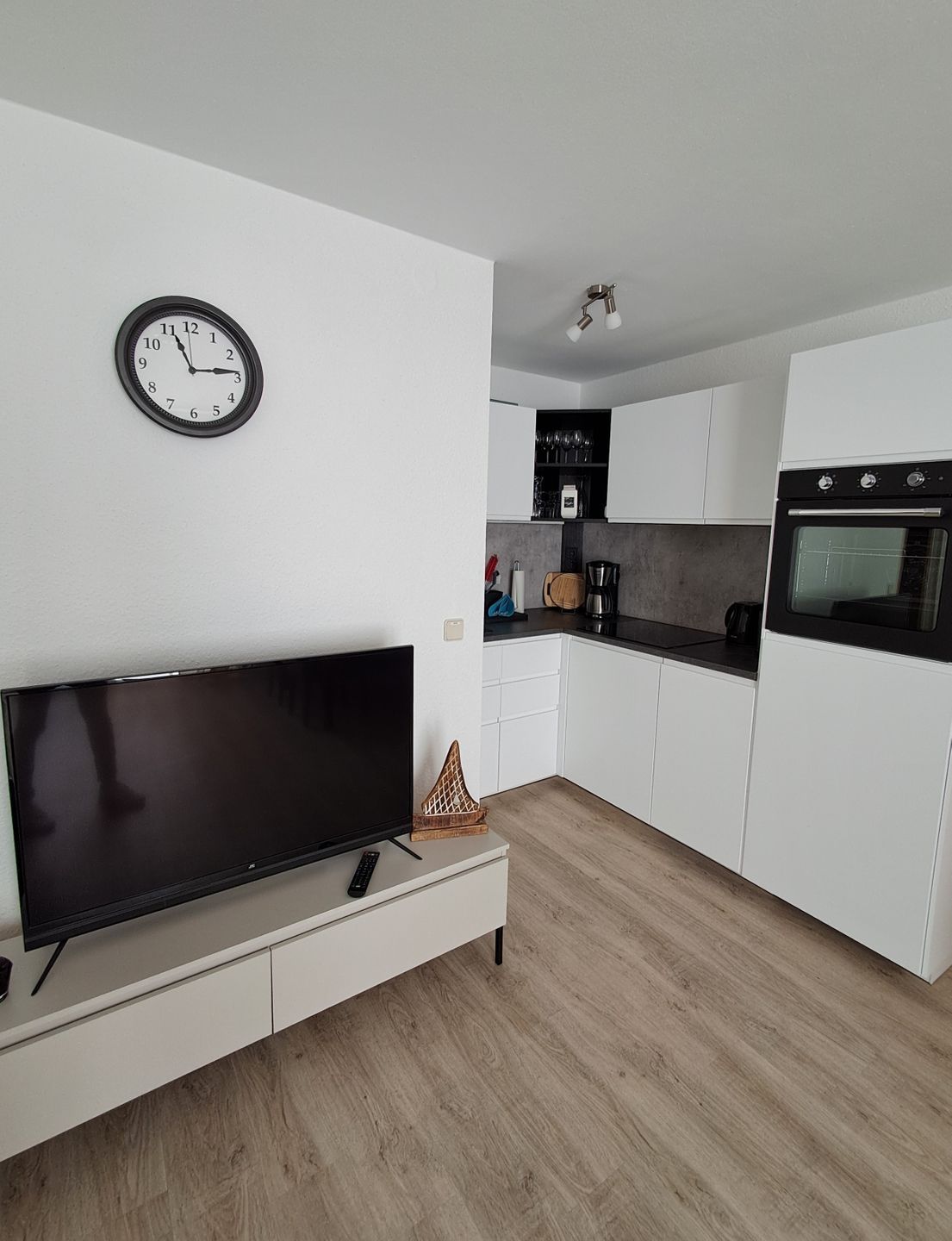 Eine moderne Küche mit weißen Schränken, einem Einbauofen und einem Flachbildfernseher auf einer weißen Konsole.