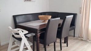 Un'area pranzo con un tavolo in legno scuro, quattro sedie nere, un'altalena per bambini, un cesto intrecciato, una lampada a sospensione e un quadro incorniciato appeso al muro.