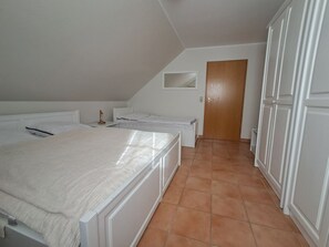 A bedroom with a large bed, a small bedside table, a wooden door, and white walls.