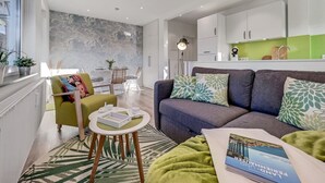 A modern living room with a grey sofa, green armchair, and a round coffee table. There is a dining area in the background with a table and chairs. - 1003 - Lütt Wulkjes - Lütt Wulkjes - Nordic charm (Dahme)