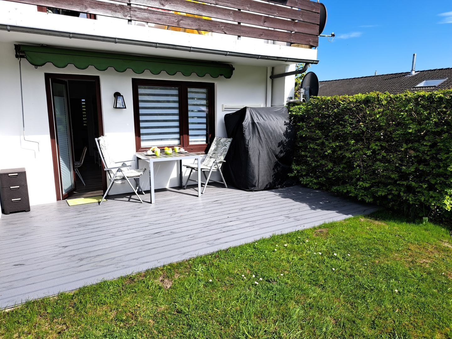 Une terrasse avec une table et des chaises, un espace abrité et une haie.