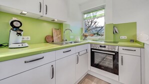 A modern kitchen with white cabinets, a green countertop, a coffee machine, a sink, and an oven. - 1003 - Lütt Wulkjes - Lütt Wulkjes - Nordic charm (Dahme)